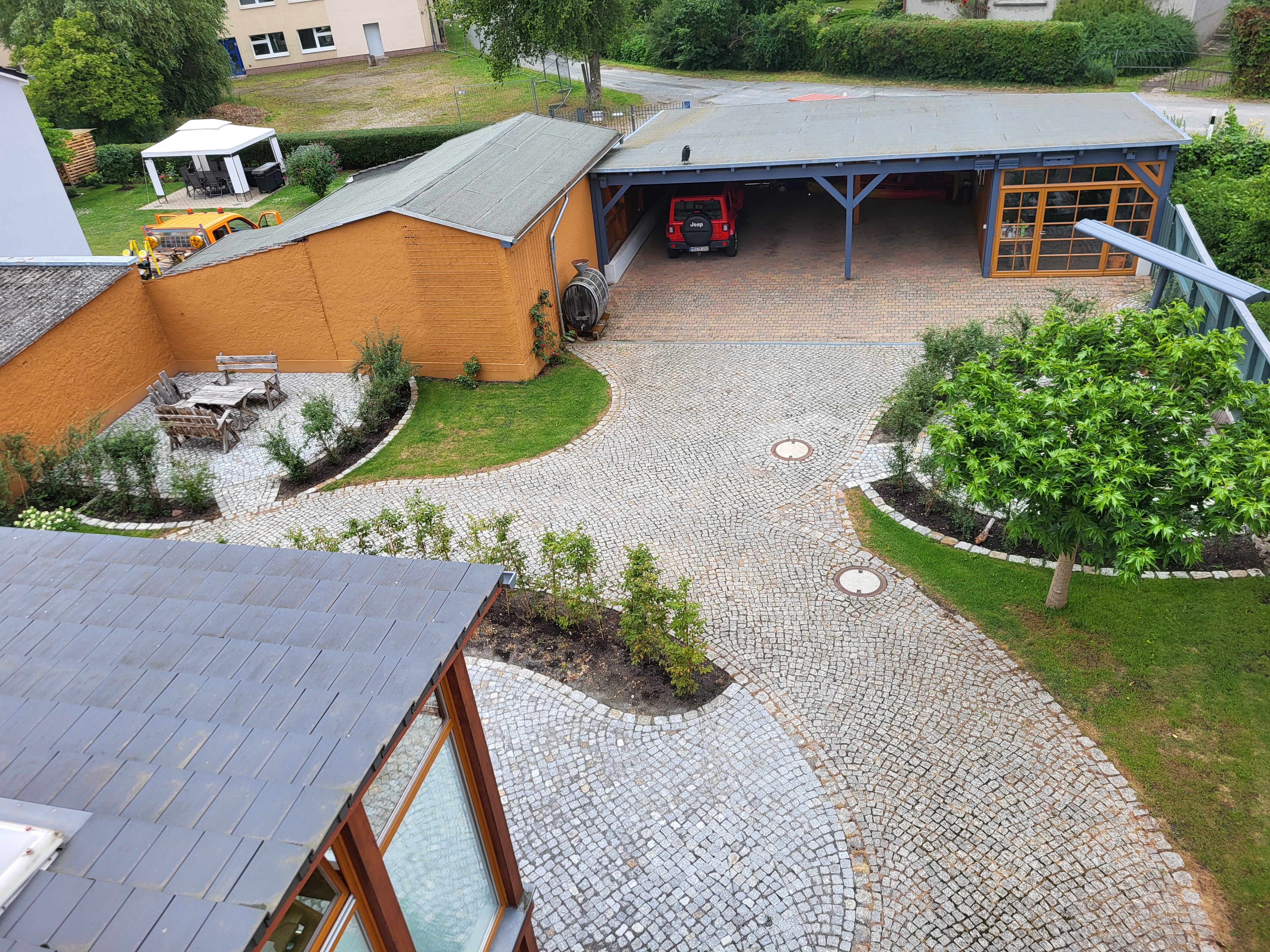 Luftaufnahme des Grundstücks in Neubrandenburg mit überdachtem Carport, geparktem Auto, gepflastertem Innenhof und angrenzendem Garten der Zeitwohnung