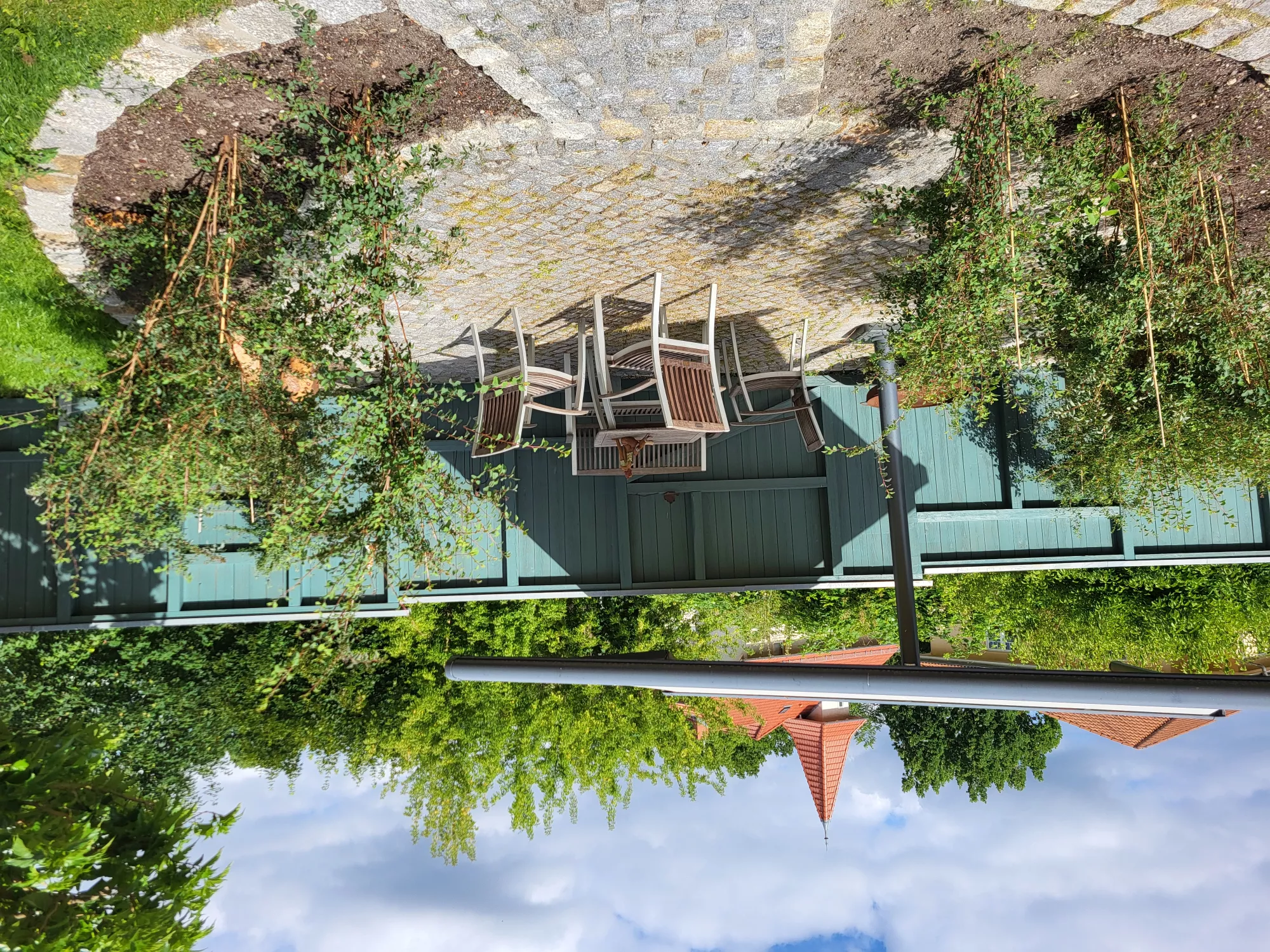 Private Gartenterrasse der Zeitwohnung in Neubrandenburg mit Teak-Sitzgruppe für vier Personen vor grünem Hecken- und Baumbestand